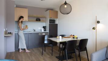 A modern kitchen with a woman preparing food, a dining table with chairs, and a sofa in the living area.