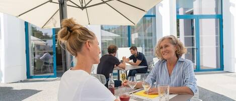 Een buitenrestaurant met tafels en parasols, een bord met de tekst