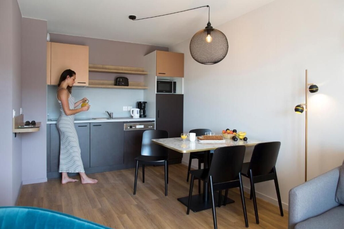A modern kitchen with grey cabinets, a black refrigerator, a coffee machine, and a dining area with a table and chairs.