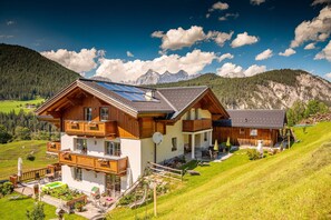 Een houten huis met twee verdiepingen, een balkon, zonnepanelen en uitzicht op bergen.