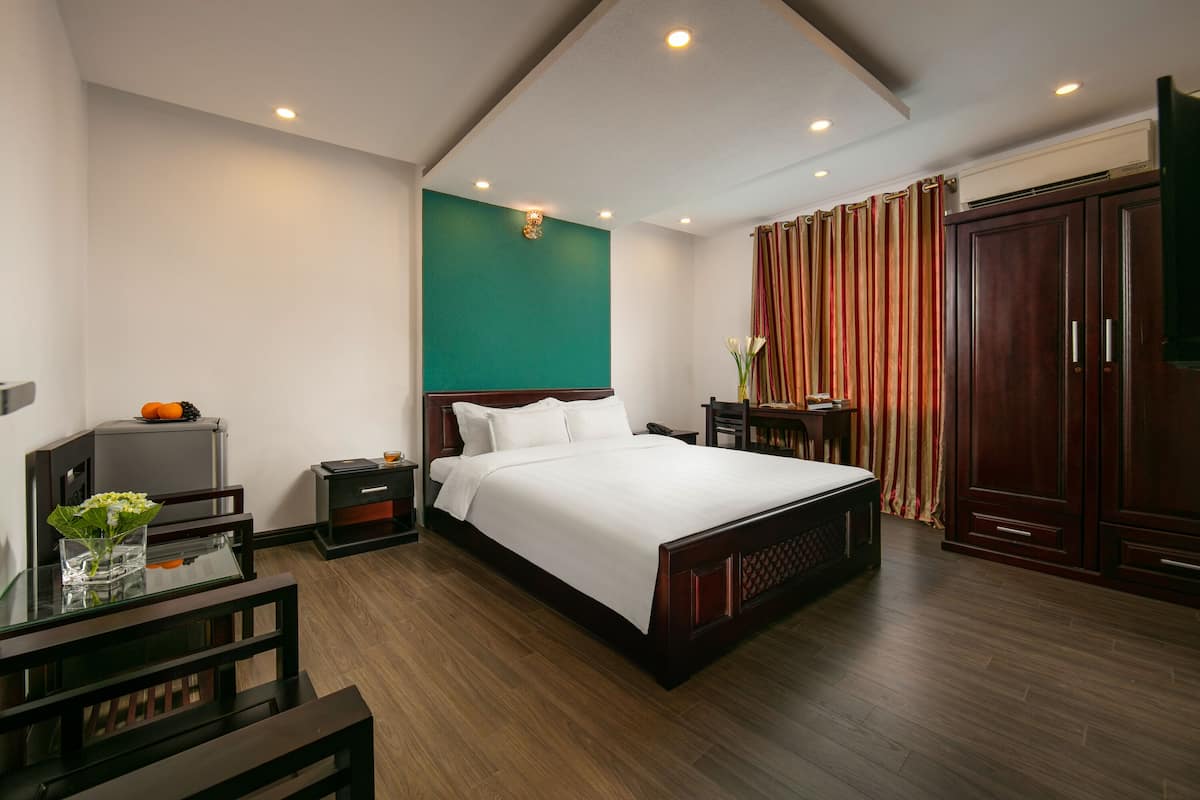 A hotel room with a large bed, a desk with a chair, a small table with a vase, and a wardrobe.