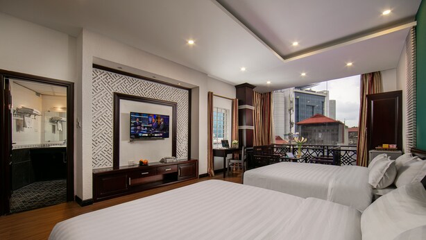 A hotel room with two beds, a TV, a desk with a chair, and a view of the city. - Duc Trong Hotel (Hanoi)