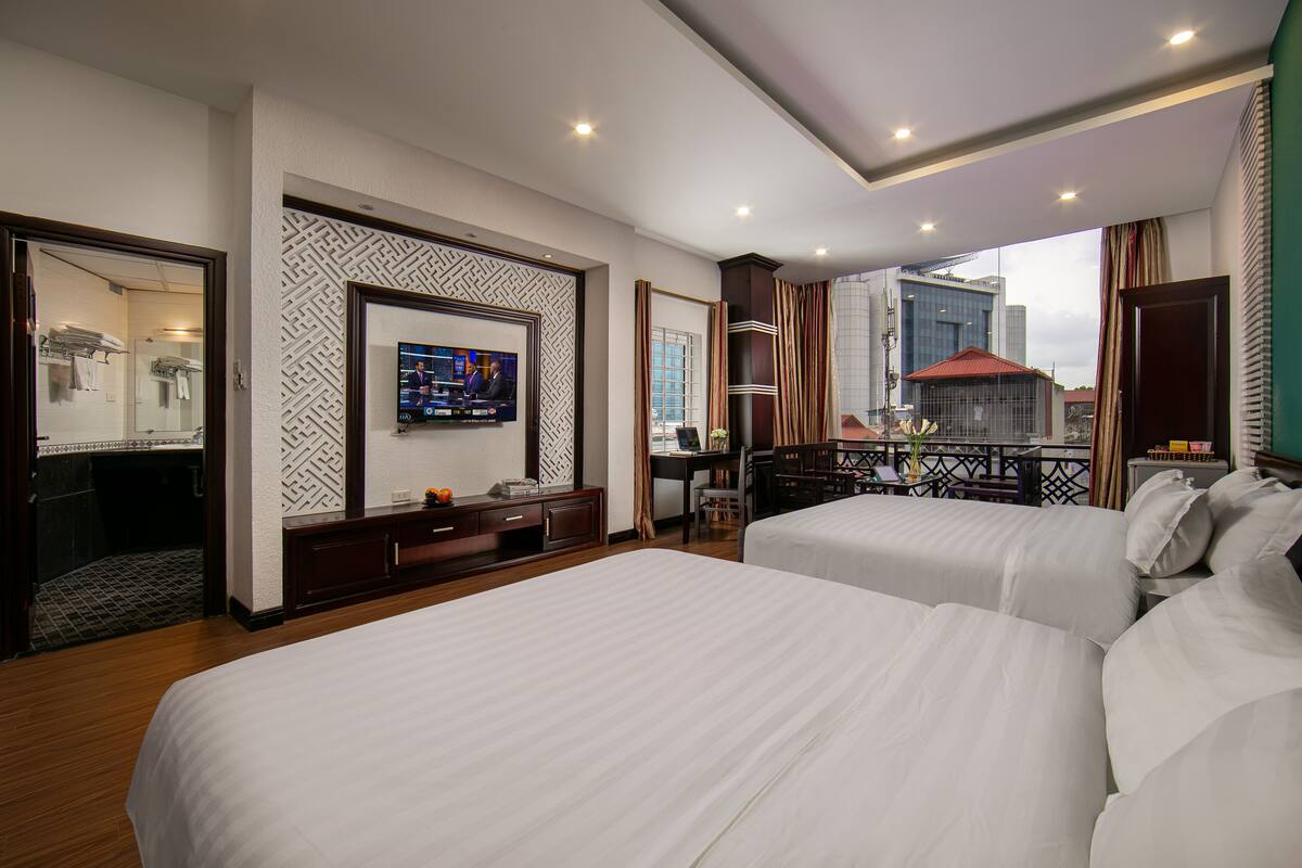 A hotel room with two beds, a TV, a desk with a chair, and a view of the city.