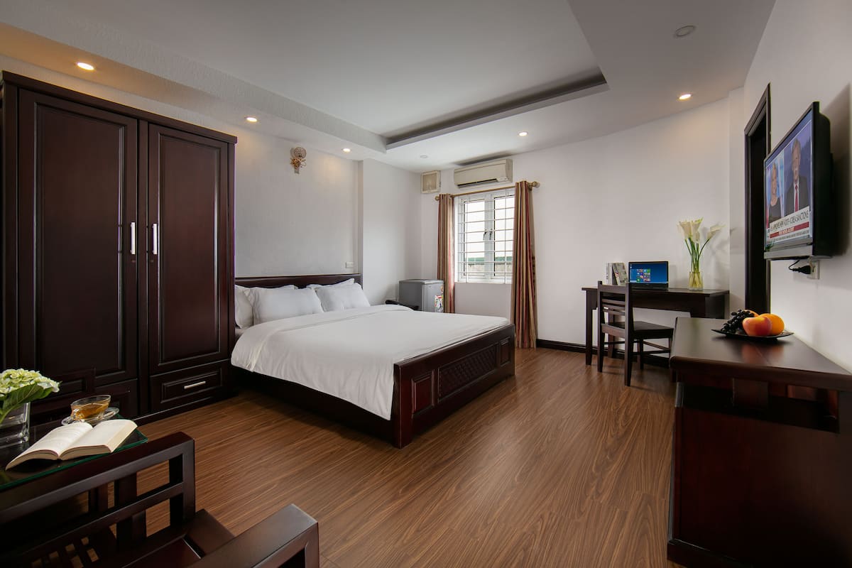 A hotel room with a large bed, a desk with a chair, a TV, and a wardrobe.