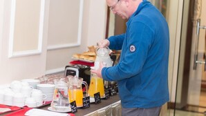 A man serving orange juice from a pitcher at a buffet table with plates and cups. - Duc Trong Hotel (Hanoi)