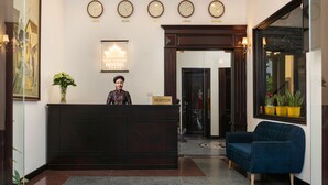 A hotel reception area with a dark reception desk, a receptionist, a reception sign, and clocks displaying times from Tokyo, Beijing, and London. - Duc Trong Hotel (Hanoi)