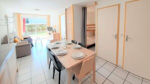 Ein Essbereich mit Tisch für vier Personen, einer Couch, einem Fernseher und Blick ins Freie.