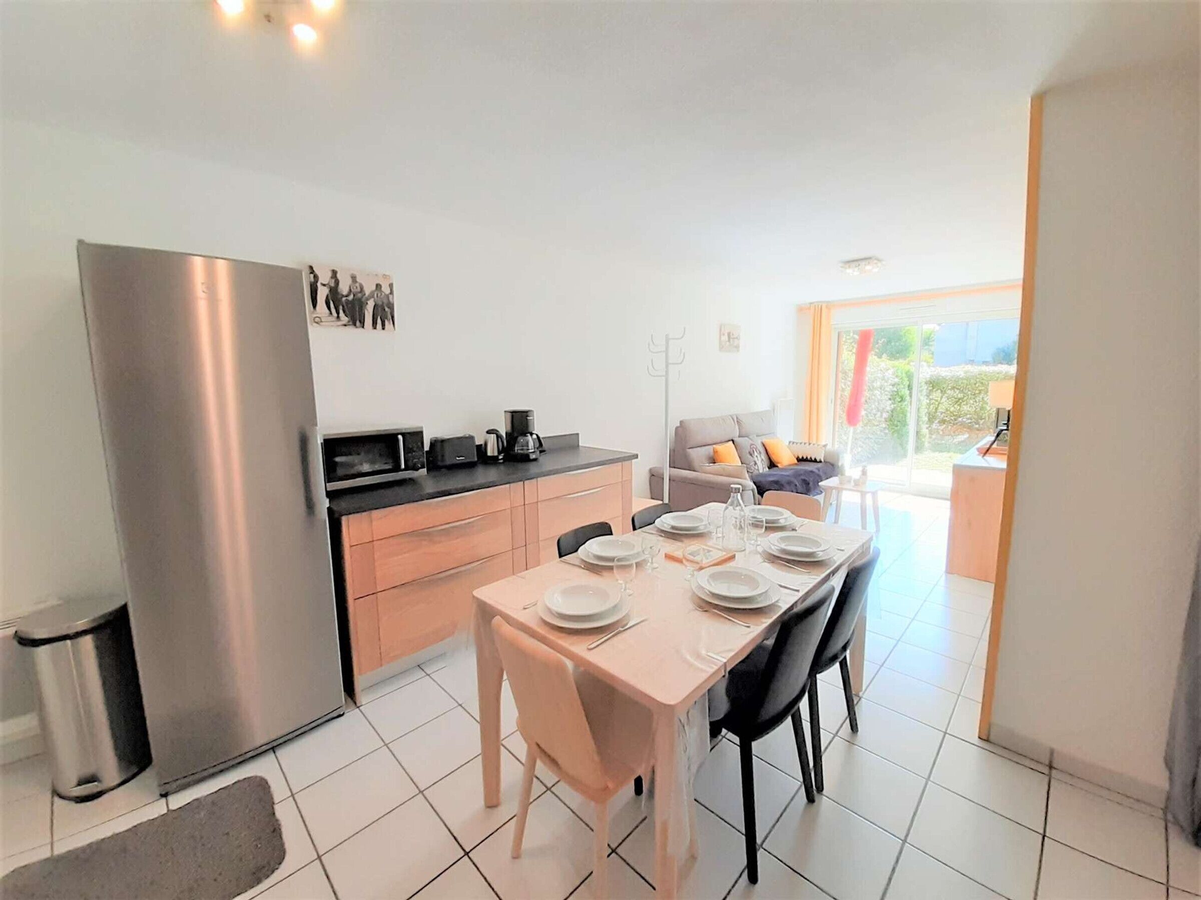 Una cocina moderna con un refrigerador de acero inoxidable, una mesa de comedor con platos y vasos, y un sofá al fondo.