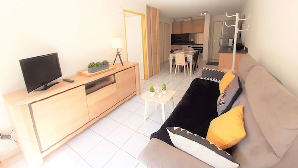 Ein modernes Wohnzimmer mit Sofa, Fernseher und einem Essbereich im Hintergrund.