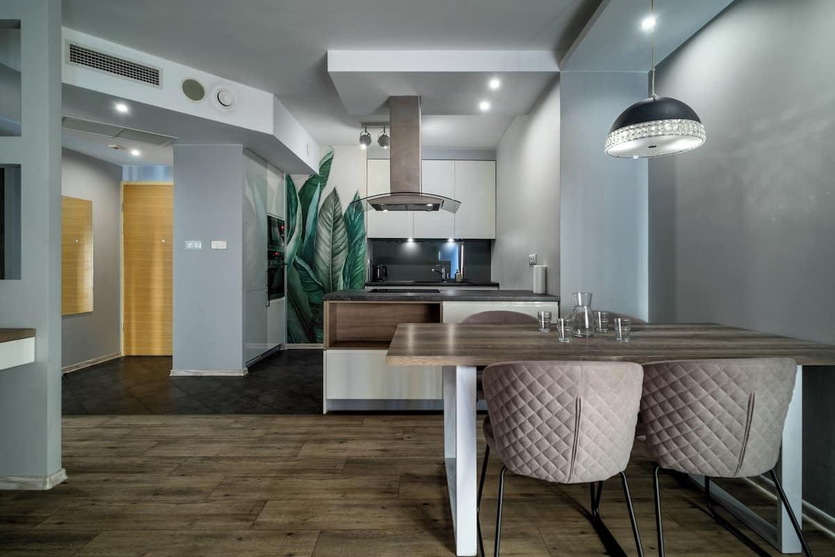 A modern kitchen with a central island, pendant lighting, and a dining area with two chairs.