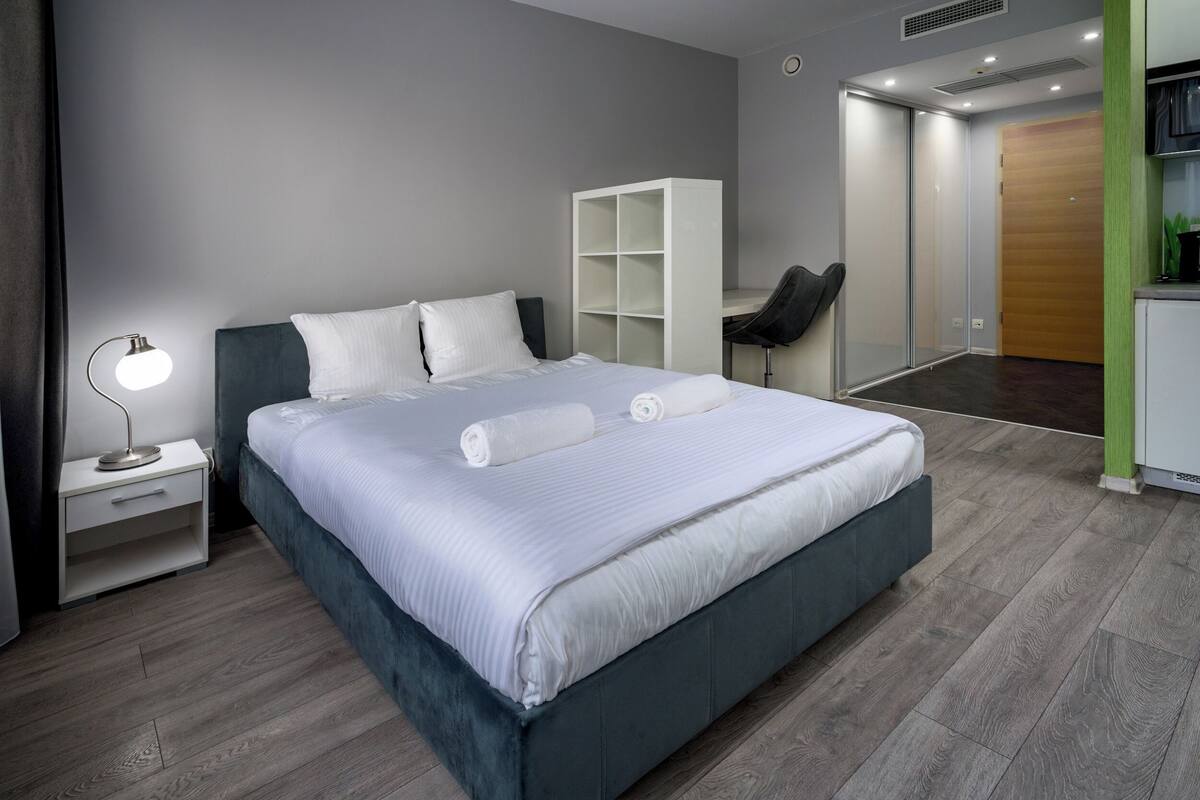 A modern bedroom with a large bed, a desk, and a wardrobe.