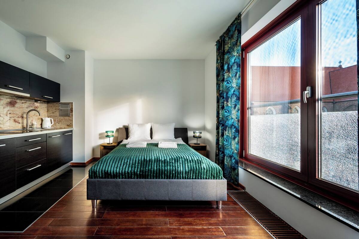 A modern bedroom with a large bed, a built-in wardrobe, a bedside table with a lamp, and a window with curtains.