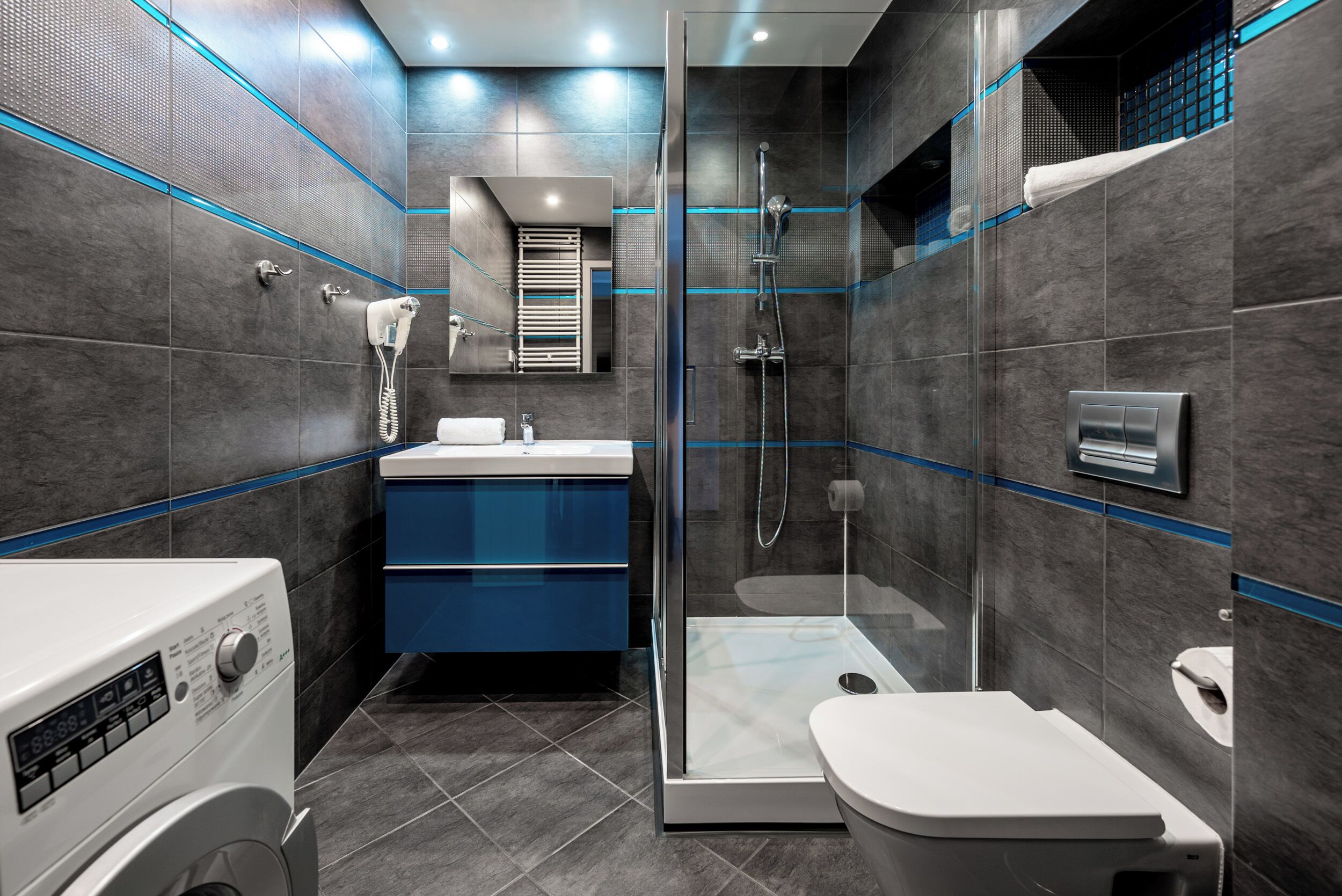Een moderne badkamer met een douchecabine van glas, een ingebouwde wasmachine en een blauwe wastafelmeubel.