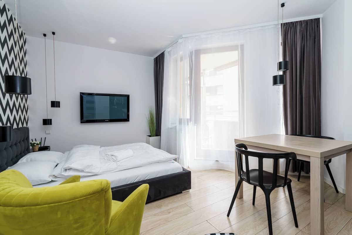 A modern hotel room with a bed, a desk, a chair, and a TV.