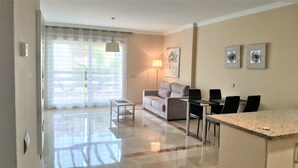 A modern living room with a sofa, a dining table with chairs, a lamp, and artwork on the wall. - El Campanario del Paraíso (Estepona)