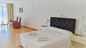 A hotel room with a large bed, a bedside table with a lamp, a chair, and a small table. - El Campanario del Paraíso (Estepona)