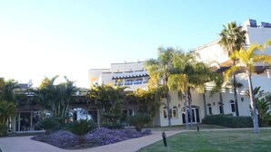A building with a modern architectural style, featuring a central courtyard with palm trees and a pathway leading to the entrance. - El Campanario del Paraíso (Estepona)