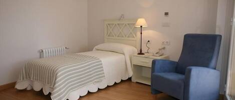 A bedroom with a bed, a chair, a nightstand, and a lamp.