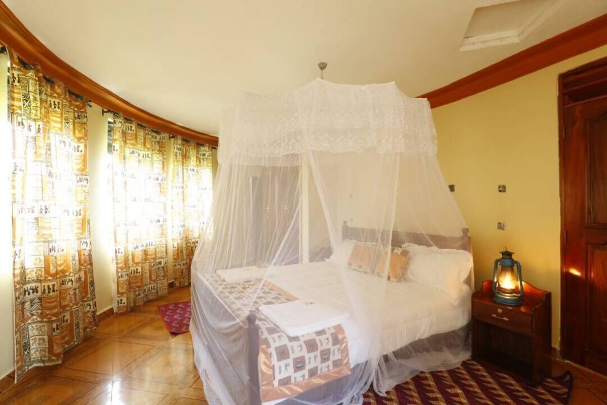 A bedroom with a canopy bed, a nightstand with a lantern, and patterned curtains.