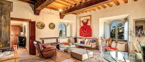 Amplia sala de estar con techo de madera, un piano, un sofá, una mesa de centro de vidrio y una mesa de comedor con sillas.