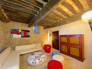 A room with a stone wall, a white sofa, a red chair, a round table with books, and a wooden door. - Torre Fortunata, Splendidly Restored Medieval Tower Near Todi in Umbria (Todi)