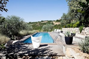 A pool area with a wooden deck, lounge chairs, and potted plants.
