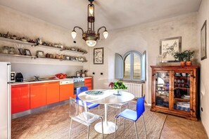 A kitchen with orange cabinets, a white dining table, and a wooden cabinet with glass doors.