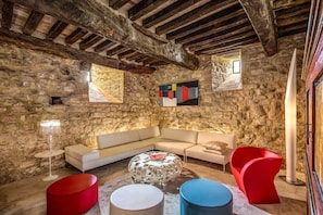 A stone-walled room with a modern sofa, red and blue chairs, and a round table.