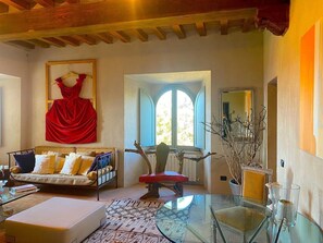 A cozy living room with a sofa, a red chair, a glass table, and a window with a view. - Torre Fortunata, Splendidly Restored Medieval Tower Near Todi in Umbria (Todi)