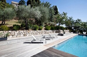 A swimming pool with a wooden deck and lounge chairs, surrounded by greenery and a stone wall. - Torre Fortunata, Splendidly Restored Medieval Tower Near Todi in Umbria (Todi)