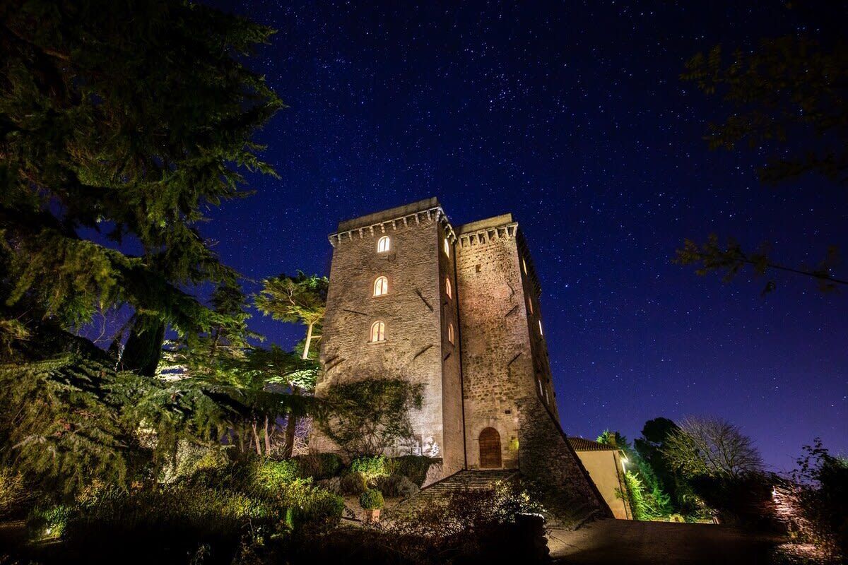 A historic stone tower with multiple windows, surrounded by trees and illuminated by artificial lighting.
