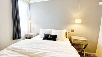 A hotel room with a large bed, two bedside tables, a nightstand, a lamp, and a window with curtains.
