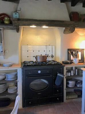 A kitchen with a black stove, white tiled backsplash, and shelves with dishes and cookware.
