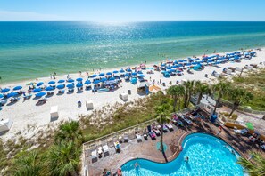 A beach resort with a swimming pool, beach umbrellas, and lounge chairs.