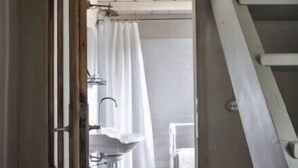 Un corridoio stretto che conduce a un bagno con un lavandino bianco e una tenda doccia.