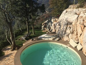 A circular pool with a stone edge, surrounded by lounge chairs and a stone wall. - Casa Stefano/ Montagne e Mare (Metato)