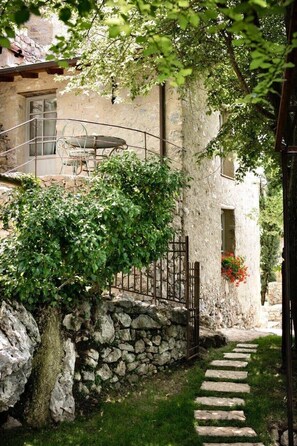 Un chemin de pierres mène à un bâtiment rustique doté d’un balcon et d’une table entourée de chaises.