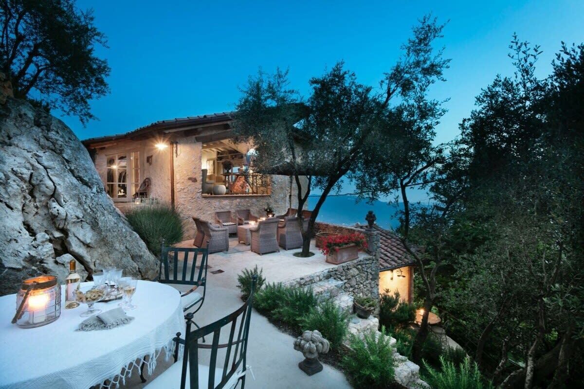A stone house with outdoor seating, a dining table, and a view of the sea.