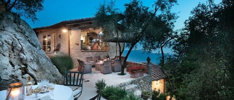 A stone house with outdoor seating, a dining table, and a view of the sea.