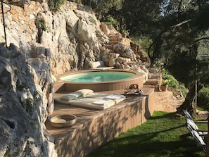 A hot tub set against a rocky backdrop with a wooden deck and lounge area. - Casa Stefano/ Montagne e Mare (Metato)