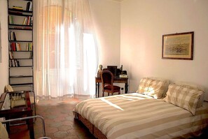 A bedroom with a bed, a desk, a chair, a bookshelf, and a window with curtains.