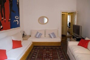 A room with a white sofa, a television, a mirror, and a patterned rug.
