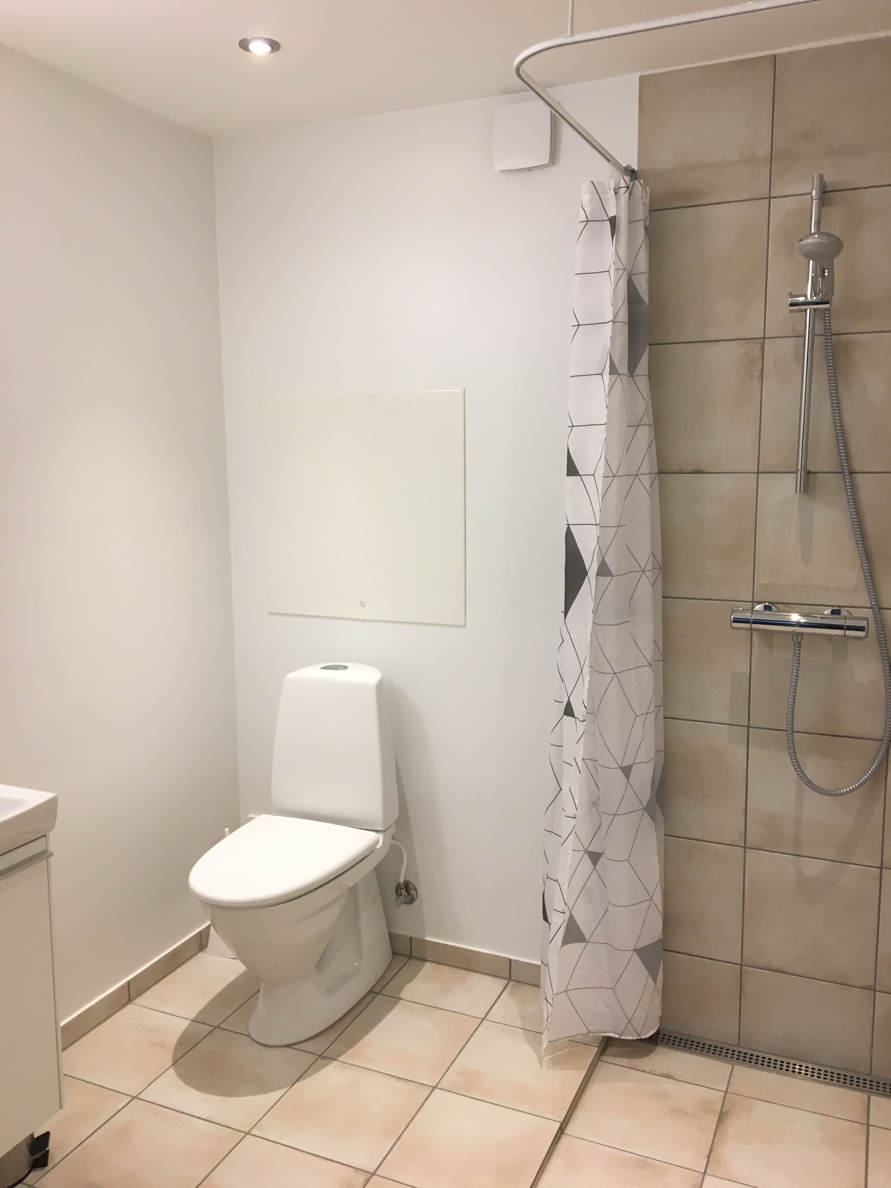 A bathroom with a toilet, shower, and tiled floor.