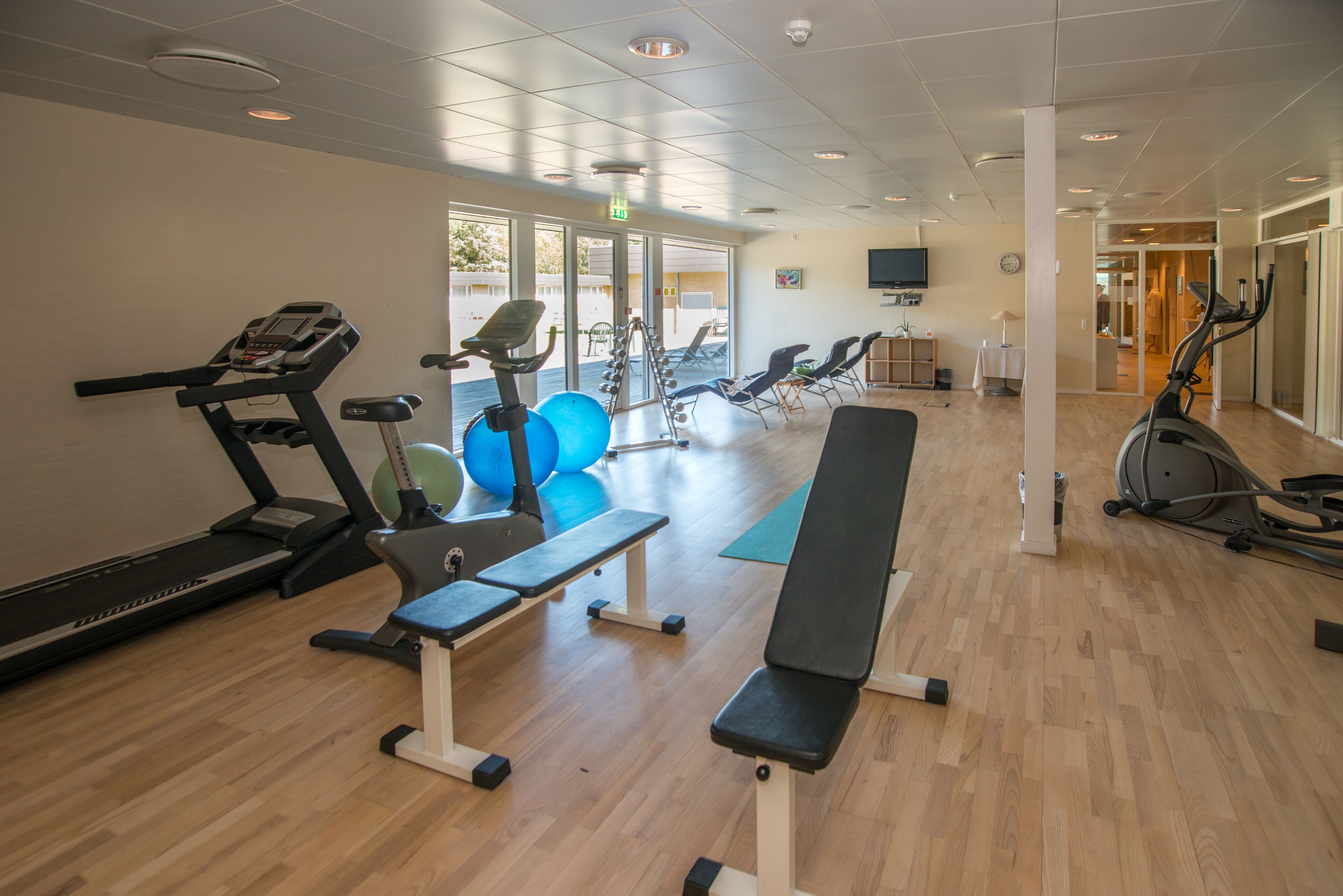 Een fitnessruimte met trainingsapparatuur, waaronder loopbanden, hometrainers en losse gewichten.
