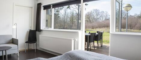 A bedroom with a large window, a bed, a chair, a table, and a radiator.