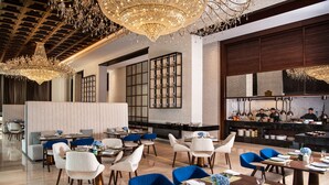 A modern restaurant with high ceilings, chandeliers, and a bar area. Tables are set with blue and white tableware. - Al Jaddaf Rotana Suite Hotel (Dubai)