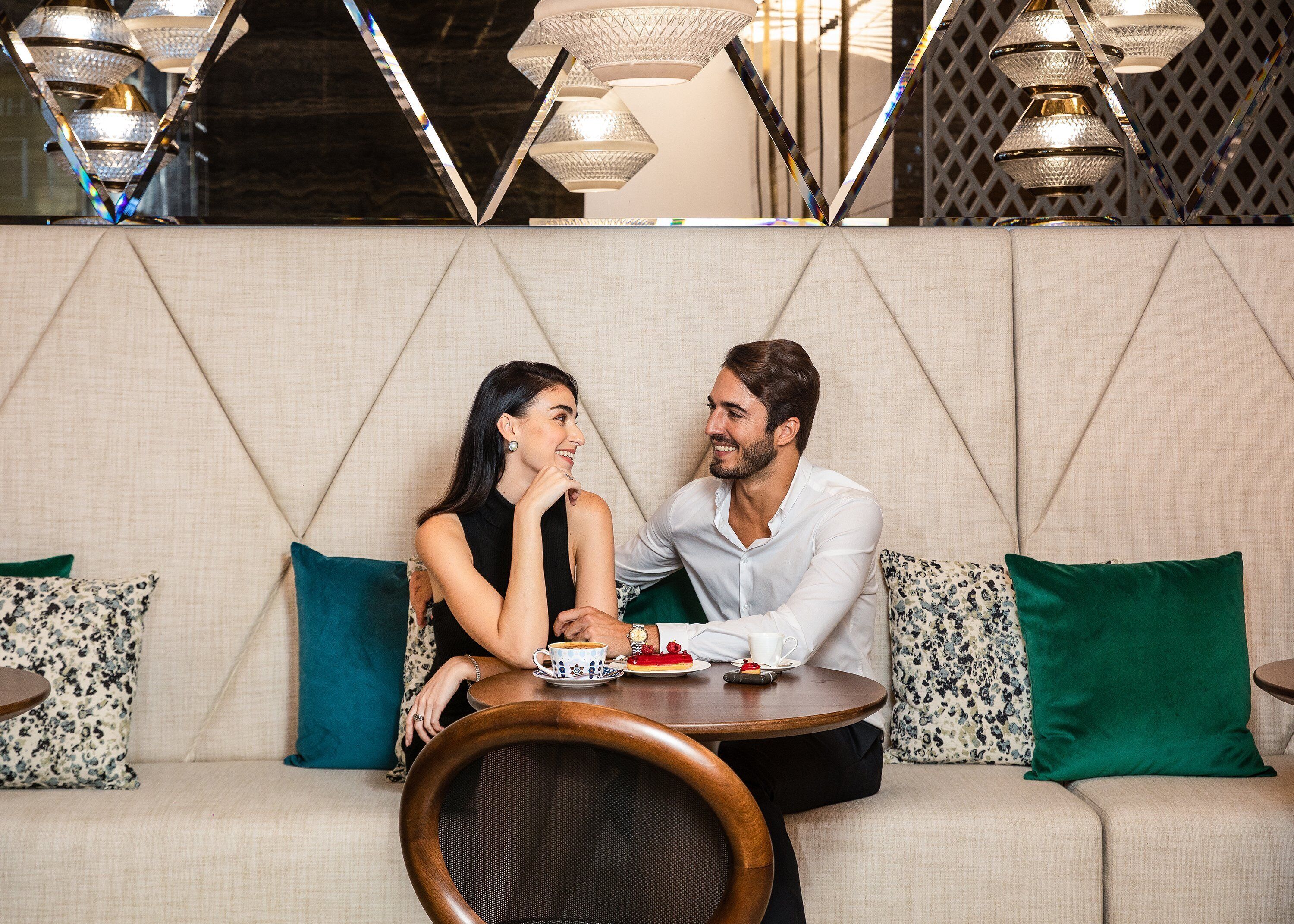 Una coppia seduta a un tavolo rotondo con un piatto di dessert in un ambiente interno moderno e ben illuminato.