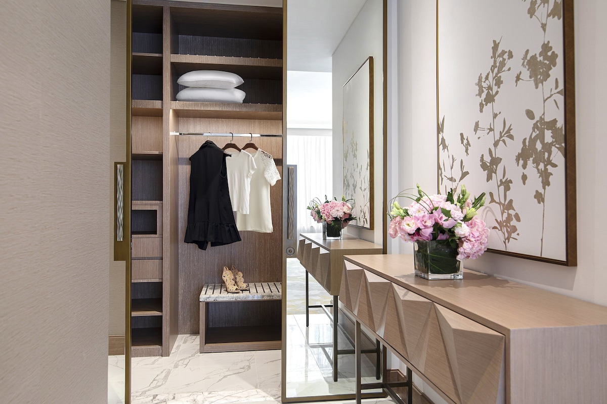 Un baño moderno con vestidor, suelo de mármol y tocador con un florero.