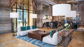 A modern lobby with a sectional sofa, a wooden coffee table, and a decorative vase with flowers. - Al Jaddaf Rotana Suite Hotel (Dubai)