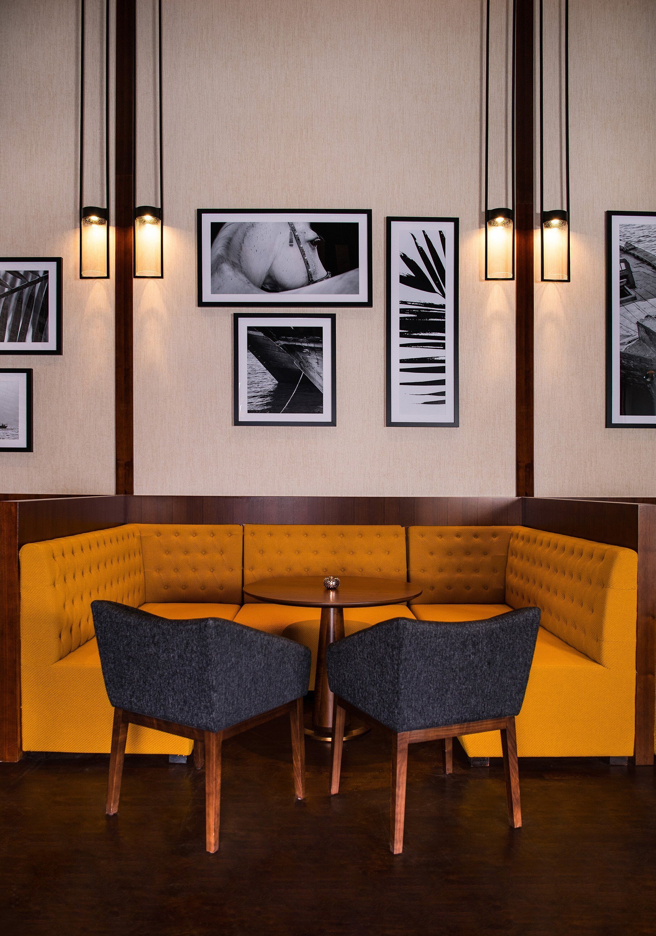 Een zithoek met een geel sofa en twee stoelen, een klein rond tafeltje, en kunstwerken in lijsten aan de muur.